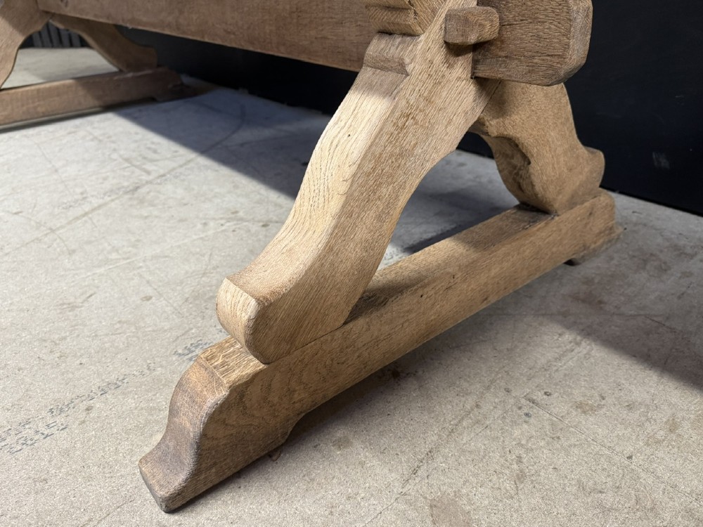 A rustic light oak dining table featuring a thick plank top supported by X-frame trestle legs and a pegged central stretcher. View XII