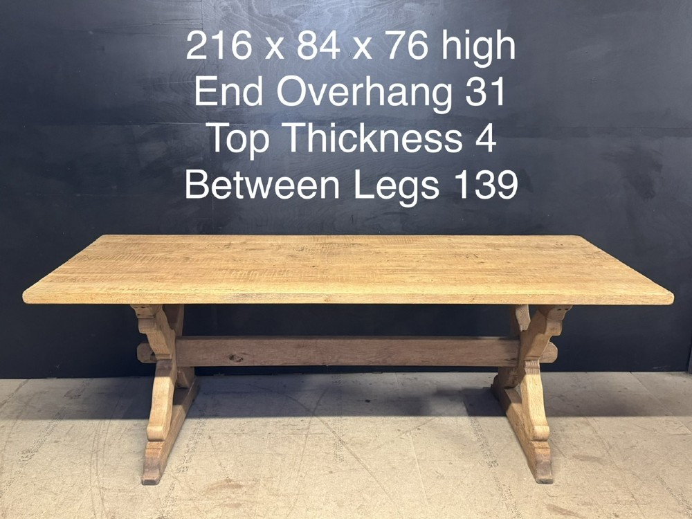 A rustic light oak dining table featuring a thick plank top supported by X-frame trestle legs and a pegged central stretcher. View XIII