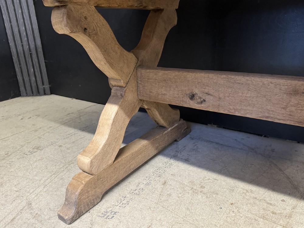 A rustic light oak dining table featuring a thick plank top supported by X-frame trestle legs and a pegged central stretcher. View XIV