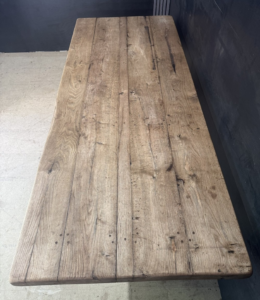 A large oak farmhouse dining table featuring a solid plank top resting on trestle end supports and a keyed stretcher. View III