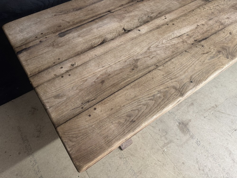 A large oak farmhouse dining table featuring a solid plank top resting on trestle end supports and a keyed stretcher. View V