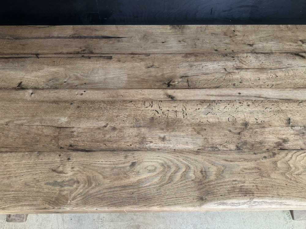 A large oak farmhouse dining table featuring a solid plank top resting on trestle end supports and a keyed stretcher. View VI
