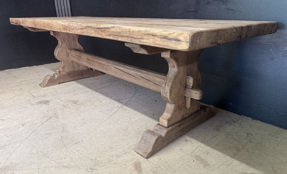 A large oak farmhouse dining table featuring a solid plank top resting on trestle end supports and a keyed stretcher. View VIII