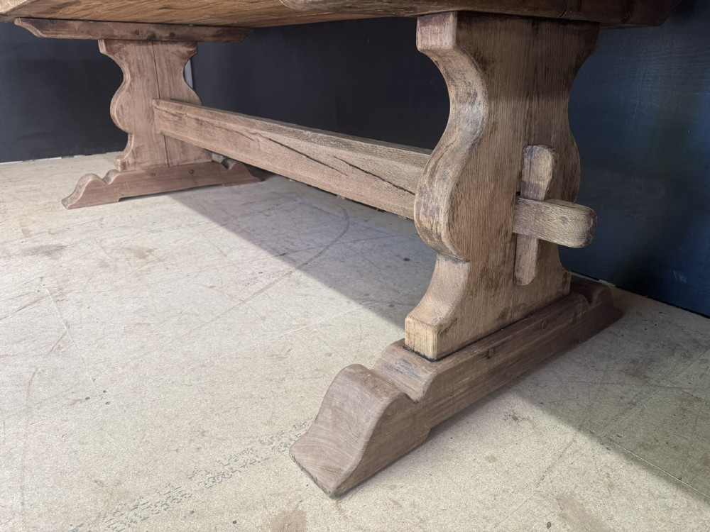 A large oak farmhouse dining table featuring a solid plank top resting on trestle end supports and a keyed stretcher. View IX