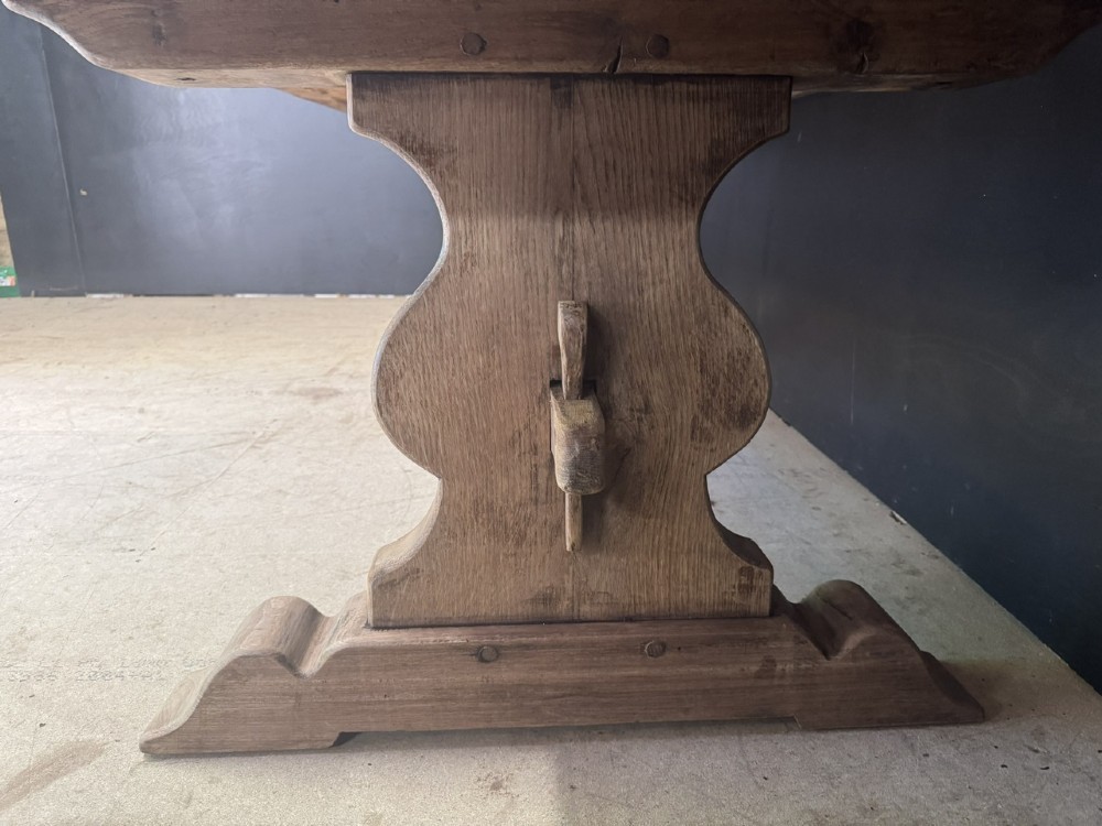A large oak farmhouse dining table featuring a solid plank top resting on trestle end supports and a keyed stretcher. View X