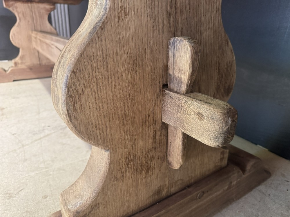 A large oak farmhouse dining table featuring a solid plank top resting on trestle end supports and a keyed stretcher. View XI