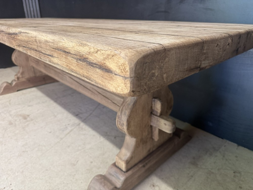 A large oak farmhouse dining table featuring a solid plank top resting on trestle end supports and a keyed stretcher. View XV