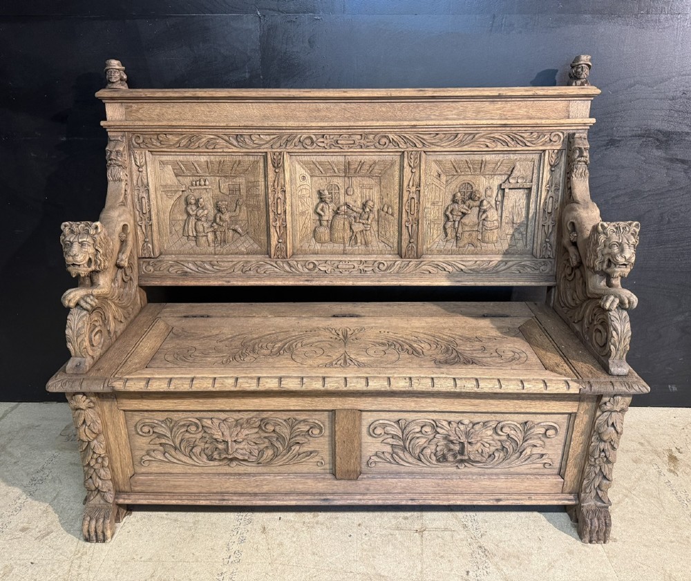 A French carved oak hall bench featuring relief panels depicting tavern scenes, lion figure armrests, and mask carvings on the base.