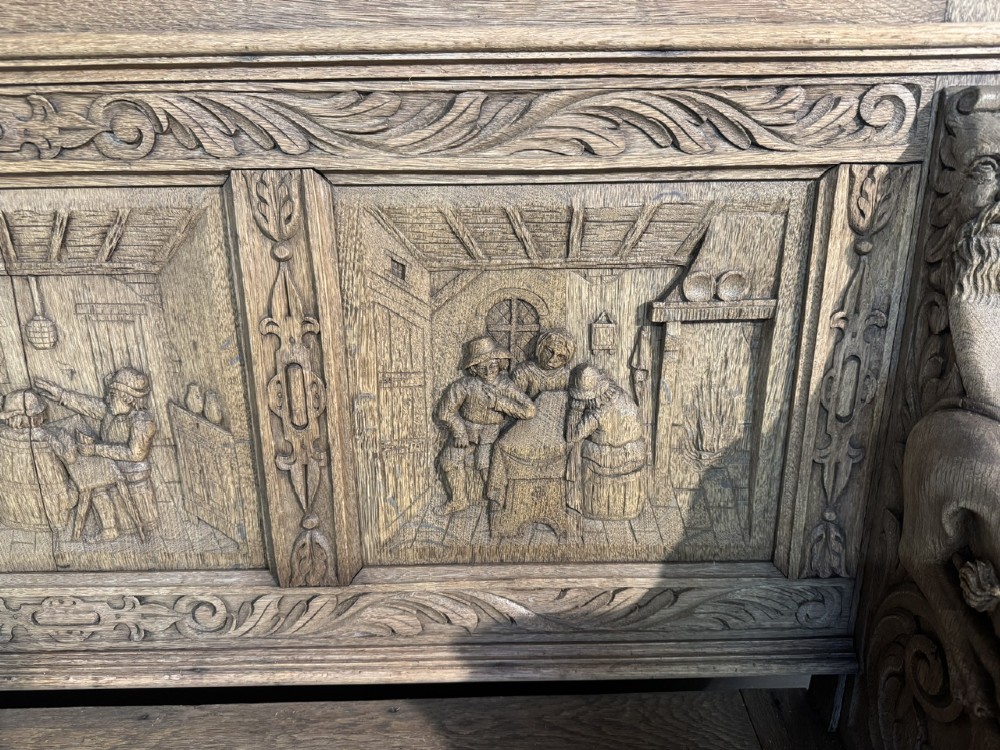 A French carved oak hall bench featuring relief panels depicting tavern scenes, lion figure armrests, and mask carvings on the base. View II