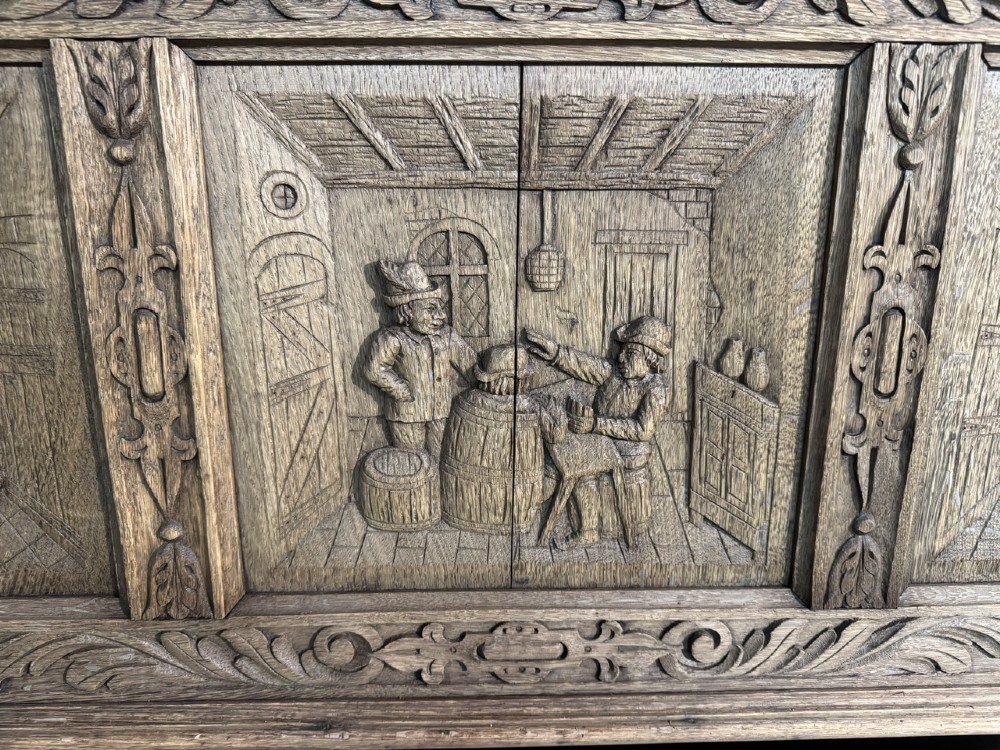 A French carved oak hall bench featuring relief panels depicting tavern scenes, lion figure armrests, and mask carvings on the base. View III