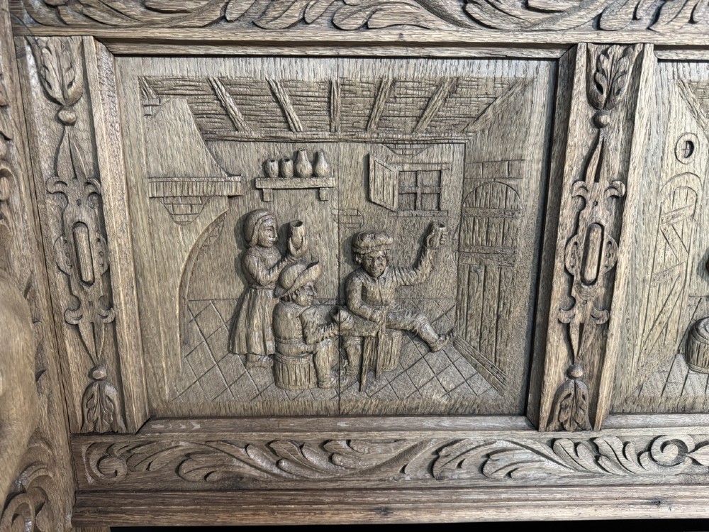 A French carved oak hall bench featuring relief panels depicting tavern scenes, lion figure armrests, and mask carvings on the base. View IV