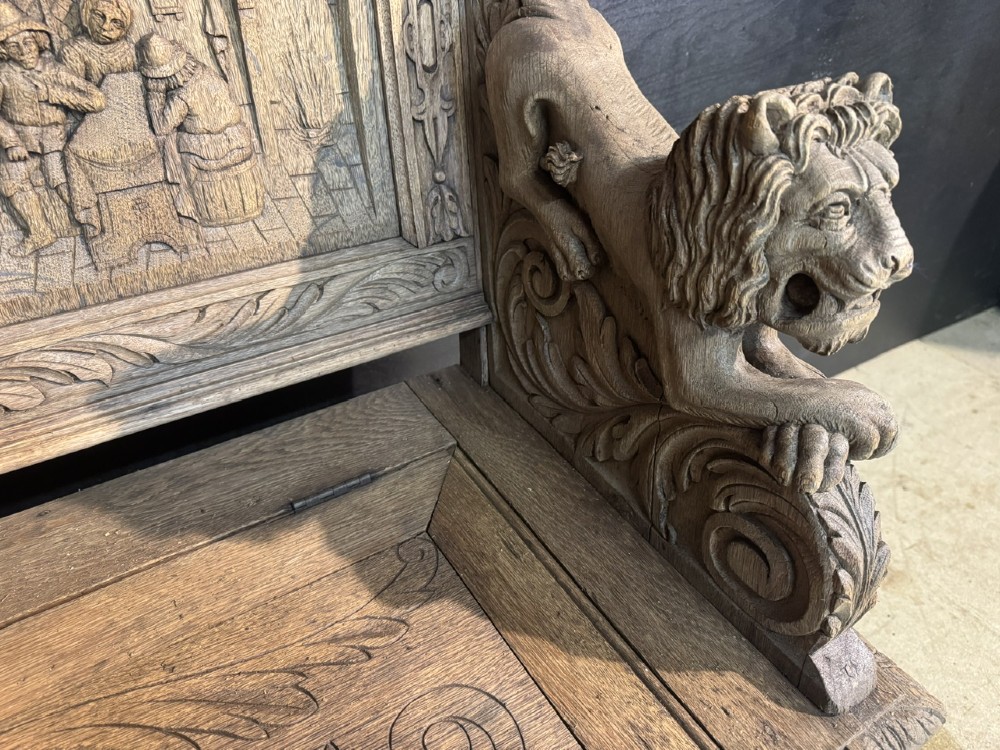 A French carved oak hall bench featuring relief panels depicting tavern scenes, lion figure armrests, and mask carvings on the base. View VI