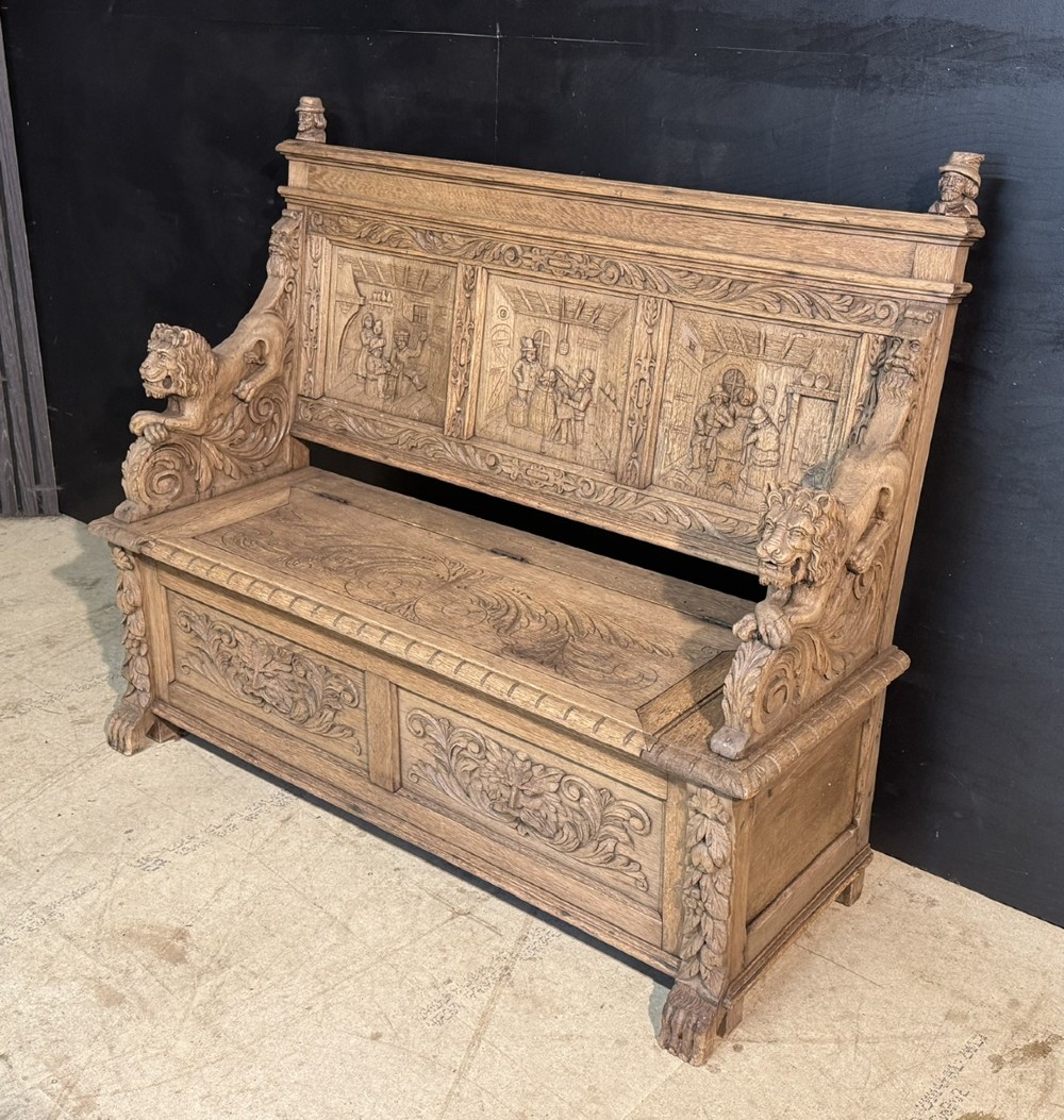 A French carved oak hall bench featuring relief panels depicting tavern scenes, lion figure armrests, and mask carvings on the base. View VIII