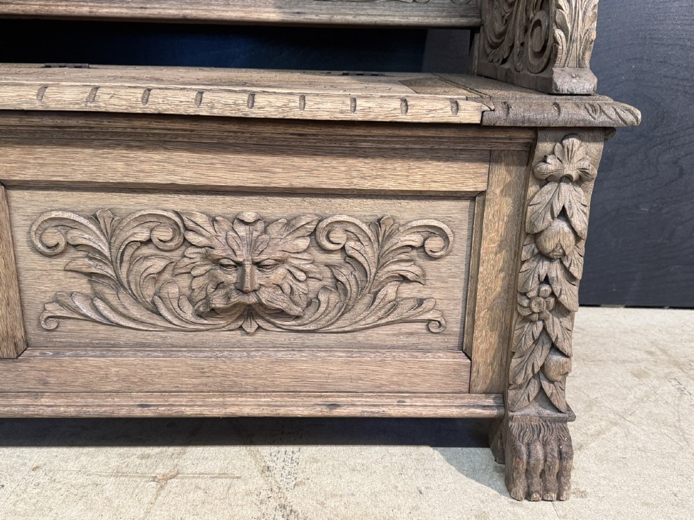 A French carved oak hall bench featuring relief panels depicting tavern scenes, lion figure armrests, and mask carvings on the base. View IX