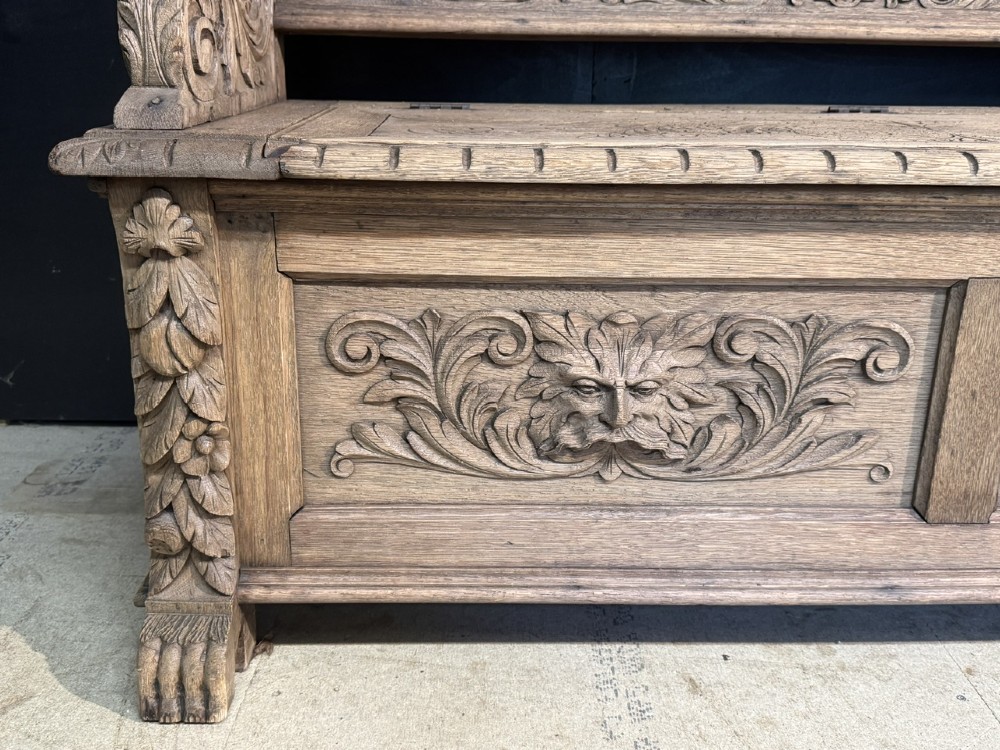 A French carved oak hall bench featuring relief panels depicting tavern scenes, lion figure armrests, and mask carvings on the base. View X