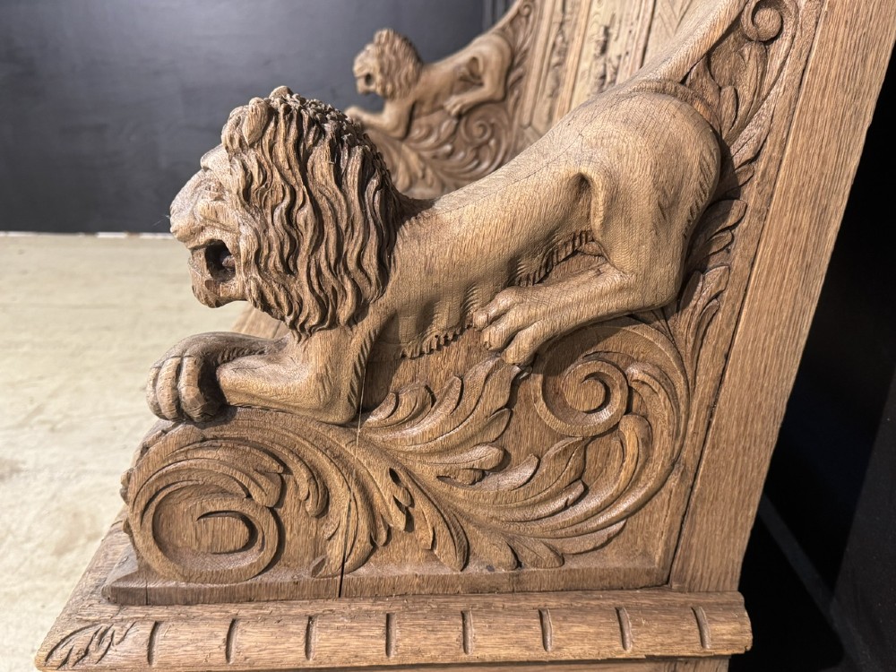 A French carved oak hall bench featuring relief panels depicting tavern scenes, lion figure armrests, and mask carvings on the base. View XII