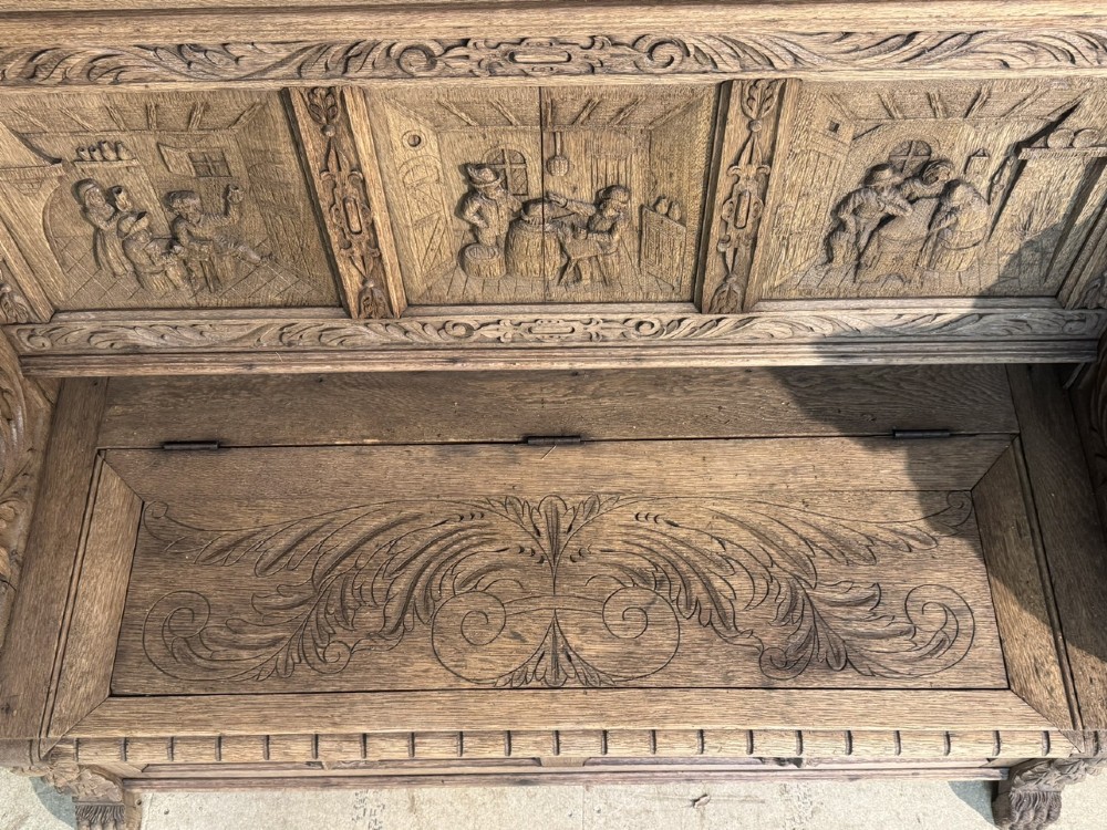 A French carved oak hall bench featuring relief panels depicting tavern scenes, lion figure armrests, and mask carvings on the base. View XIII