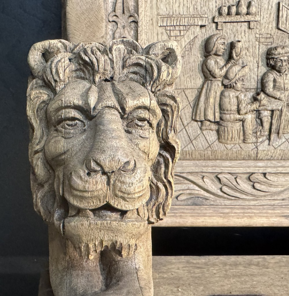 A French carved oak hall bench featuring relief panels depicting tavern scenes, lion figure armrests, and mask carvings on the base. View XIV
