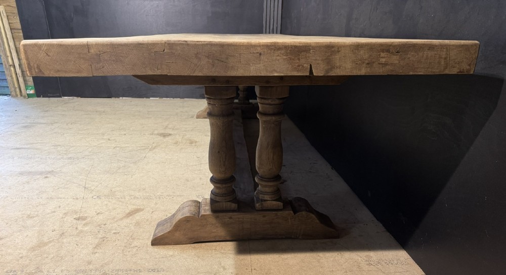 An extra long natural oak refectory dining table featuring a timber plank top supported by twin turned baluster trestle legs connected by a floor-level stretcher. View IV