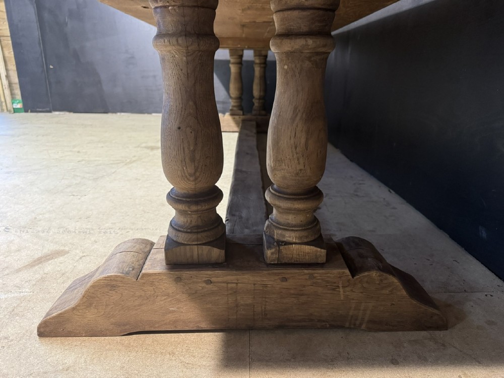 An extra long natural oak refectory dining table featuring a timber plank top supported by twin turned baluster trestle legs connected by a floor-level stretcher. View V