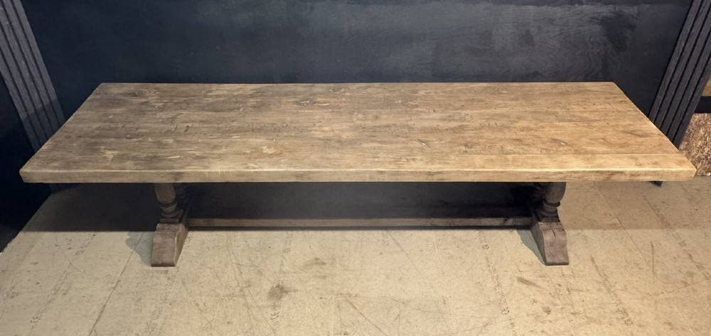 An extra long natural oak refectory dining table featuring a timber plank top supported by twin turned baluster trestle legs connected by a floor-level stretcher. View X