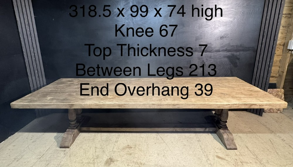 An extra long natural oak refectory dining table featuring a timber plank top supported by twin turned baluster trestle legs connected by a floor-level stretcher. View XIII
