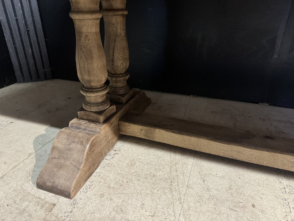 An extra long natural oak refectory dining table featuring a timber plank top supported by twin turned baluster trestle legs connected by a floor-level stretcher. View XV