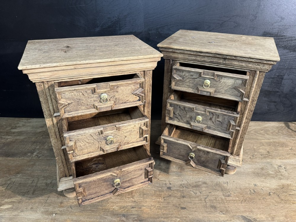 A pair of light oak three-drawer bedside chests with geometric carved drawer fronts, brass ring handles, and turned bun feet. View III