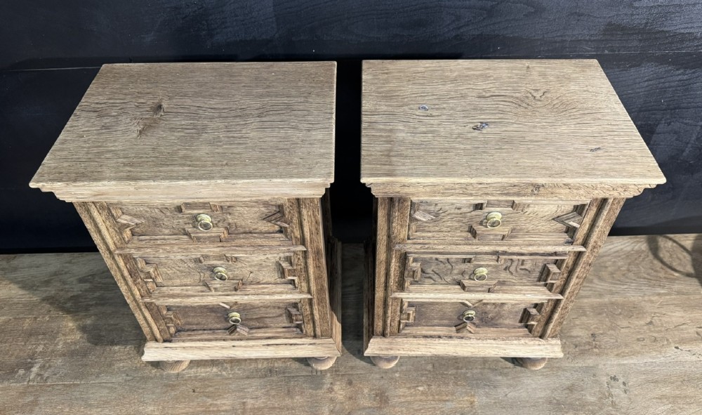 A pair of light oak three-drawer bedside chests with geometric carved drawer fronts, brass ring handles, and turned bun feet. View V