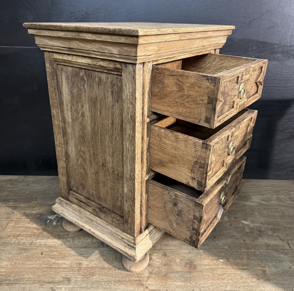 A pair of light oak three-drawer bedside chests with geometric carved drawer fronts, brass ring handles, and turned bun feet. View VII