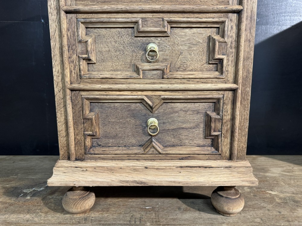 A pair of light oak three-drawer bedside chests with geometric carved drawer fronts, brass ring handles, and turned bun feet. View VIII