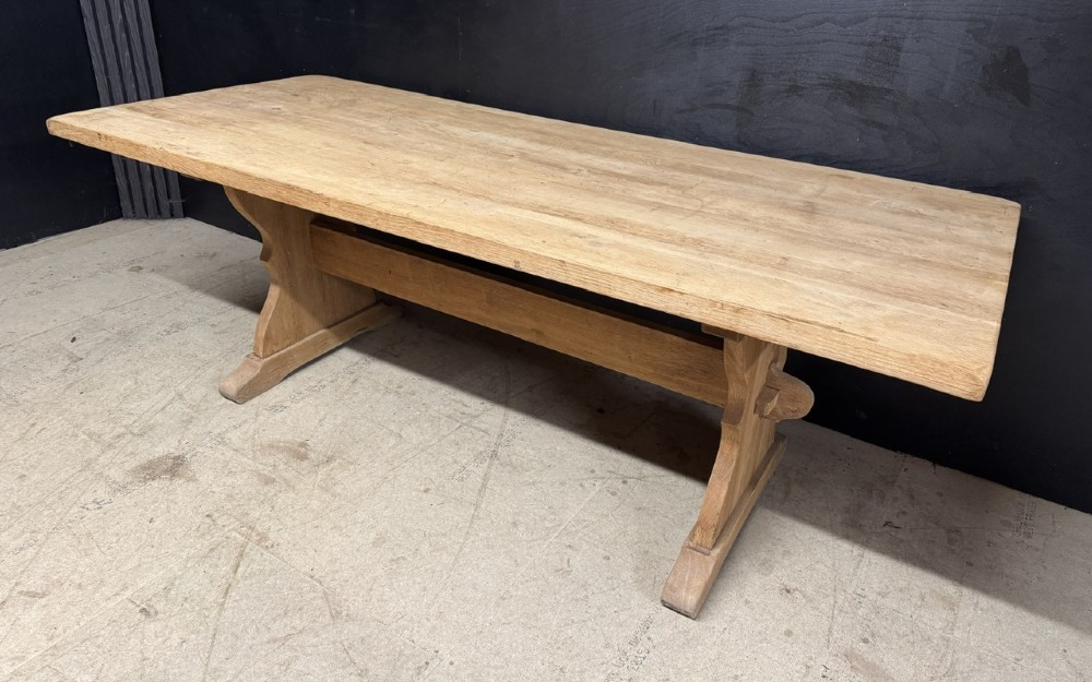 A large bleached oak farmhouse dining table featuring a thick plank top supported by a trestle base with a centre stretcher.