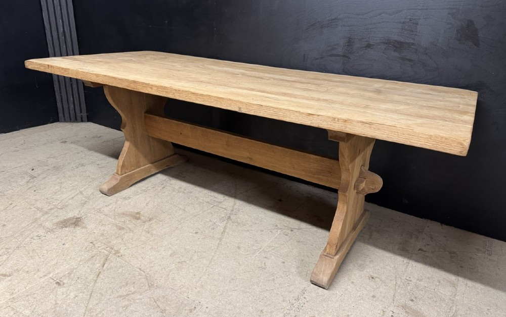 A large bleached oak farmhouse dining table featuring a thick plank top supported by a trestle base with a centre stretcher. View II