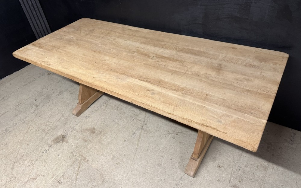 A large bleached oak farmhouse dining table featuring a thick plank top supported by a trestle base with a centre stretcher. View III