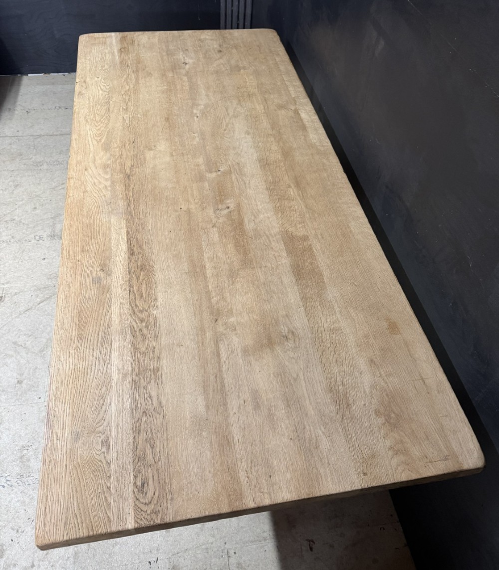 A large bleached oak farmhouse dining table featuring a thick plank top supported by a trestle base with a centre stretcher. View IV
