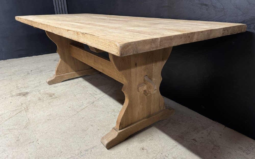 A large bleached oak farmhouse dining table featuring a thick plank top supported by a trestle base with a centre stretcher. View IX