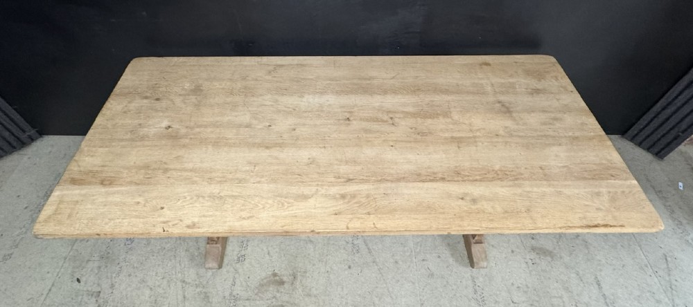 A large bleached oak farmhouse dining table featuring a thick plank top supported by a trestle base with a centre stretcher. View XII