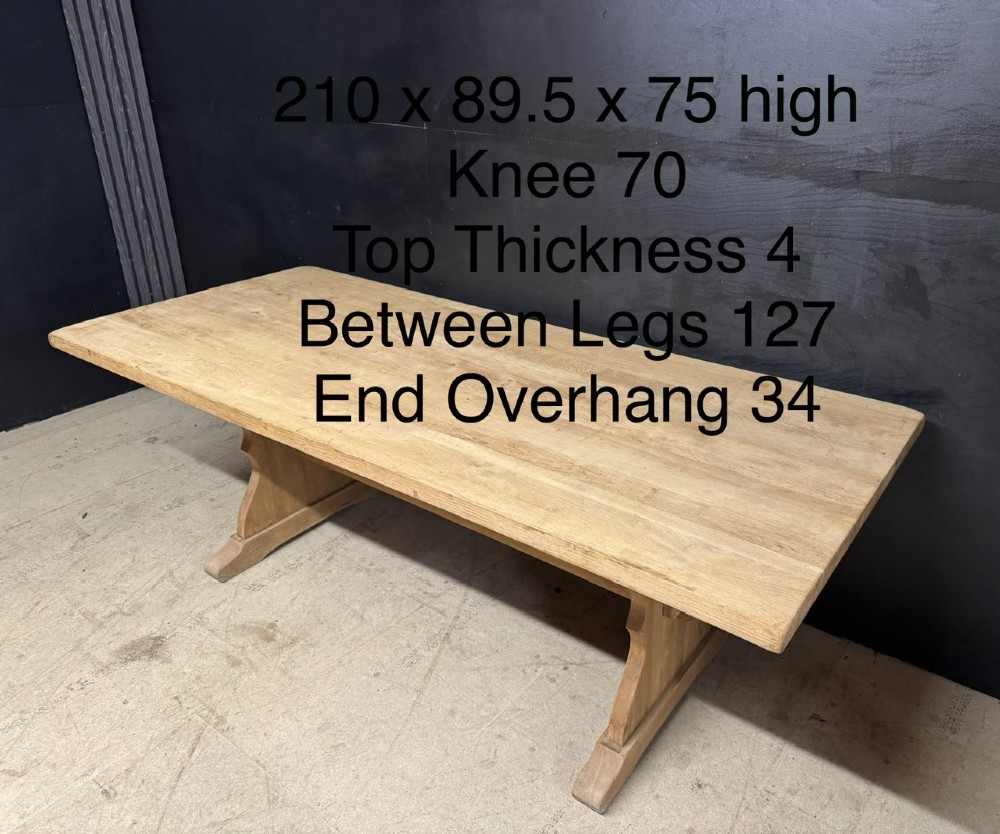 A large bleached oak farmhouse dining table featuring a thick plank top supported by a trestle base with a centre stretcher. View XIII
