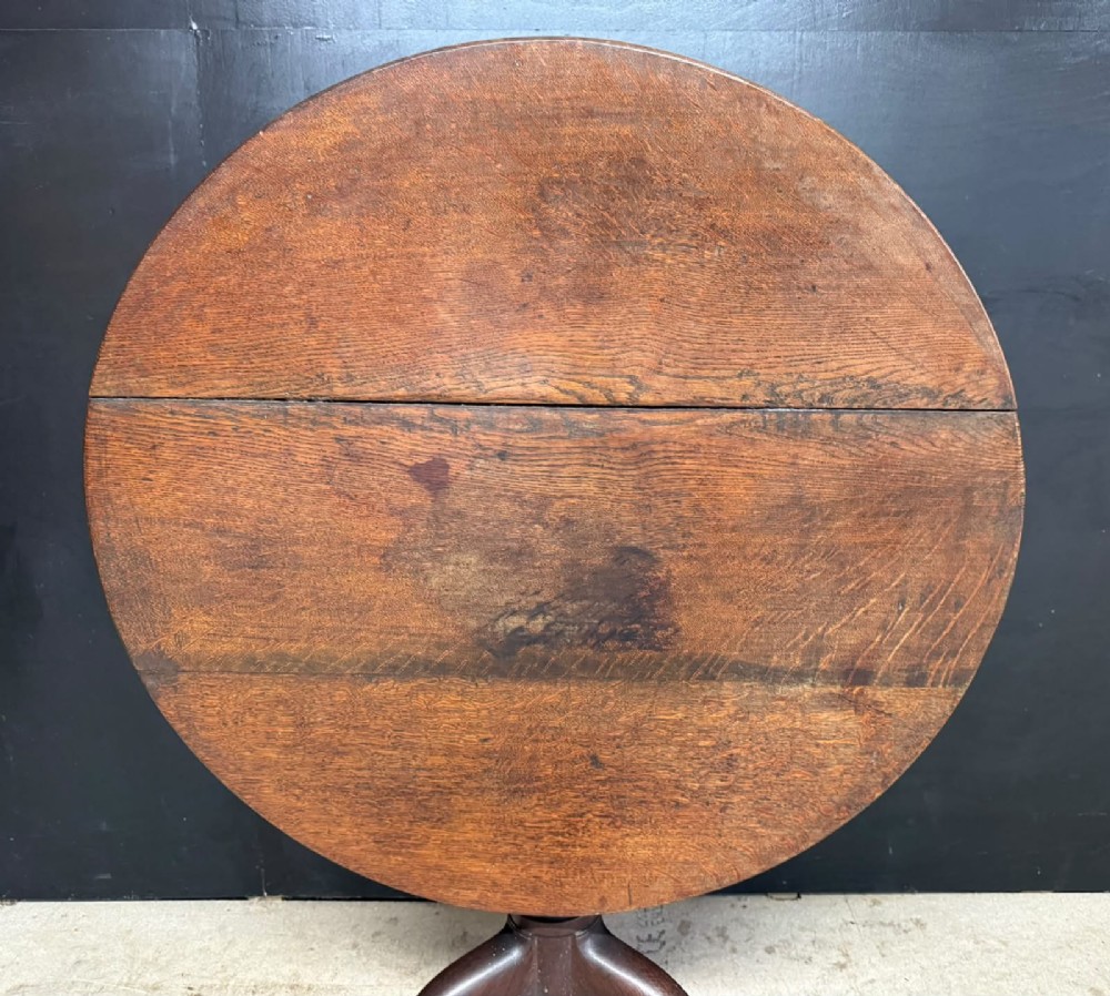 An antique circular oak tilt-top table featuring a three-plank top mounted on a turned pedestal column with three curved tripod legs. View II