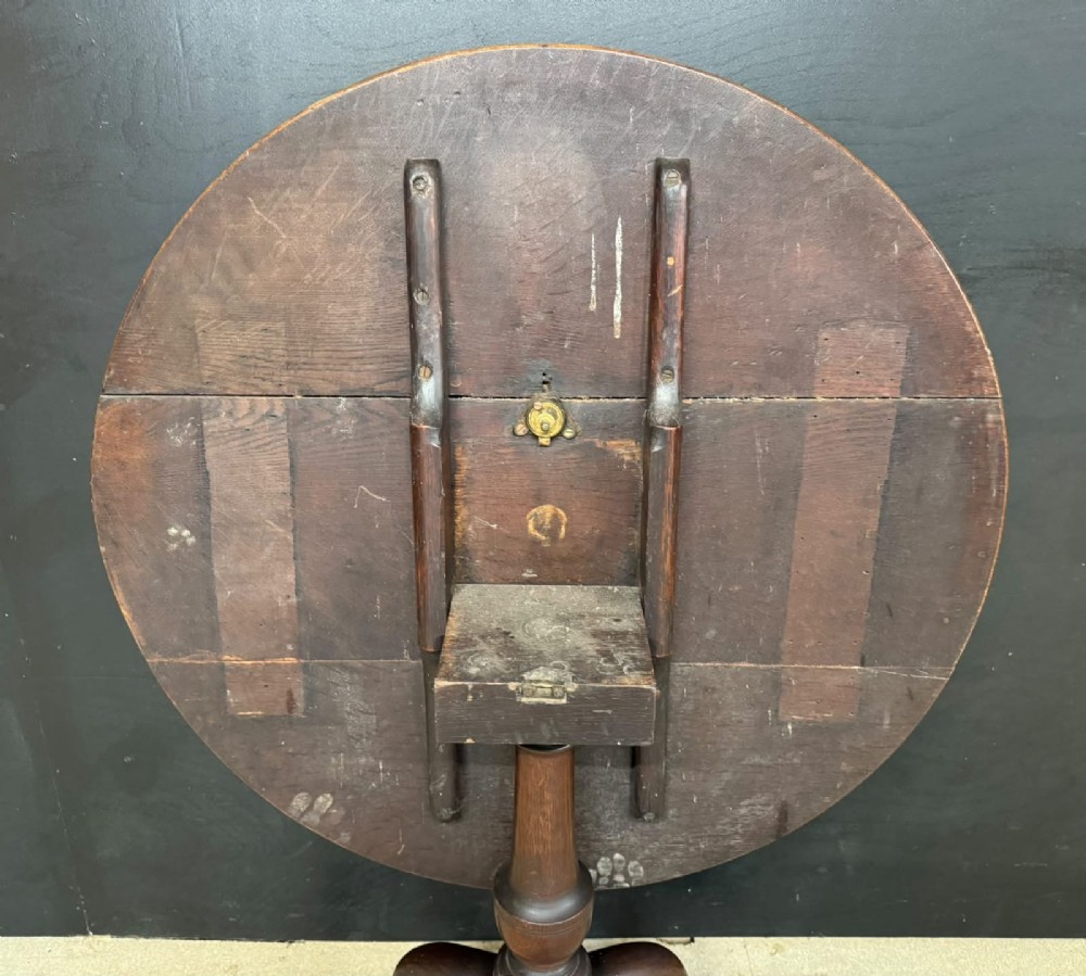 An antique circular oak tilt-top table featuring a three-plank top mounted on a turned pedestal column with three curved tripod legs. View IV