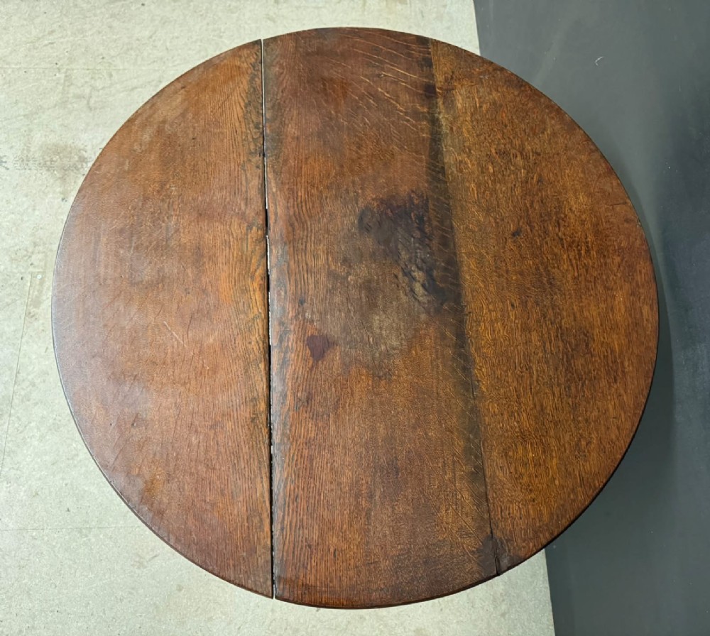 An antique circular oak tilt-top table featuring a three-plank top mounted on a turned pedestal column with three curved tripod legs. View VI