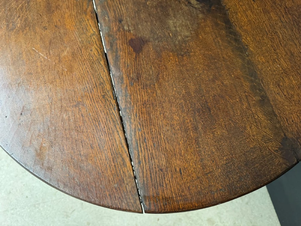 An antique circular oak tilt-top table featuring a three-plank top mounted on a turned pedestal column with three curved tripod legs. View VII