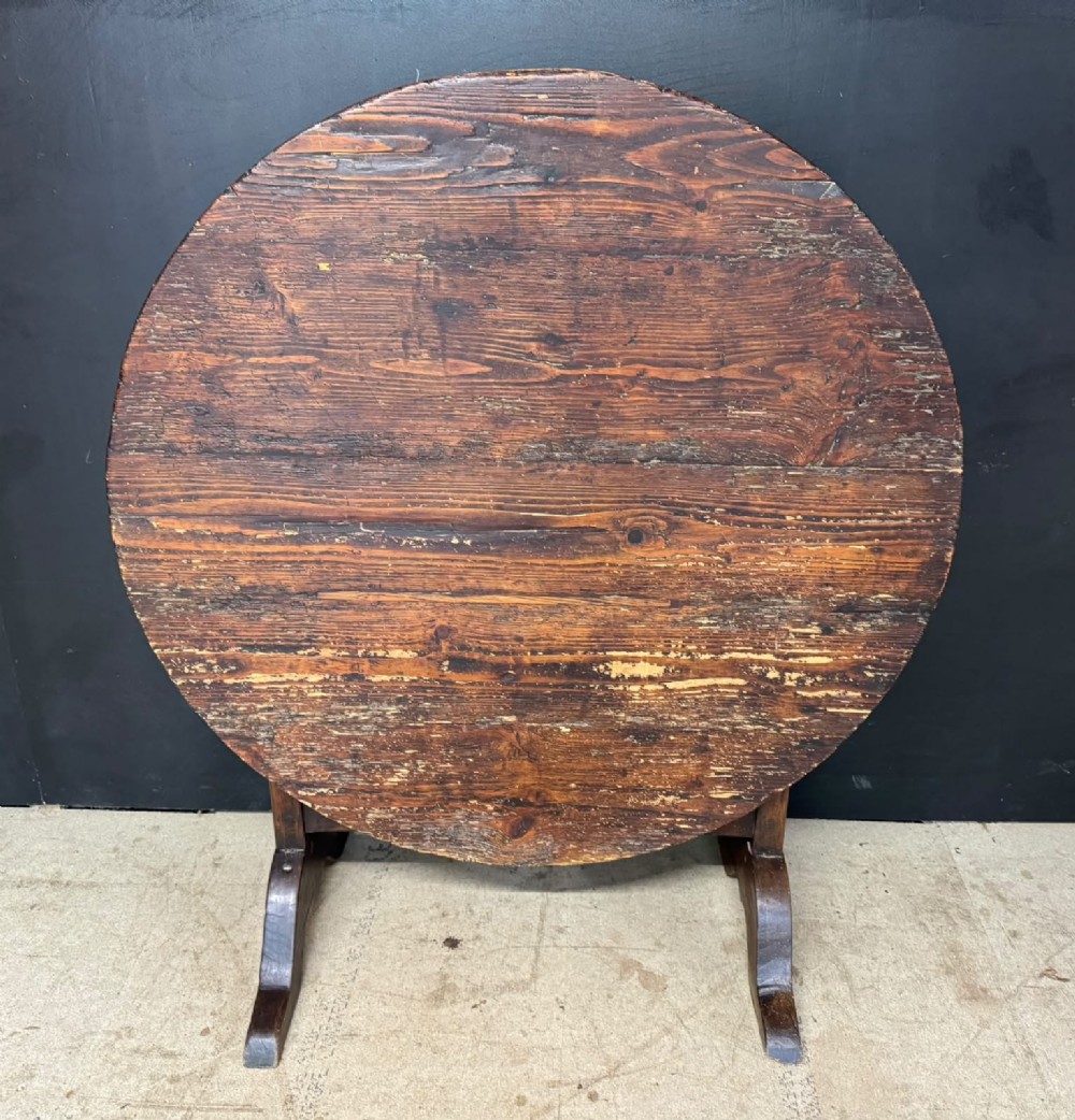 A circular French wine tasting table made of dark warm brown timber shown in a tilted position on a trestle base.