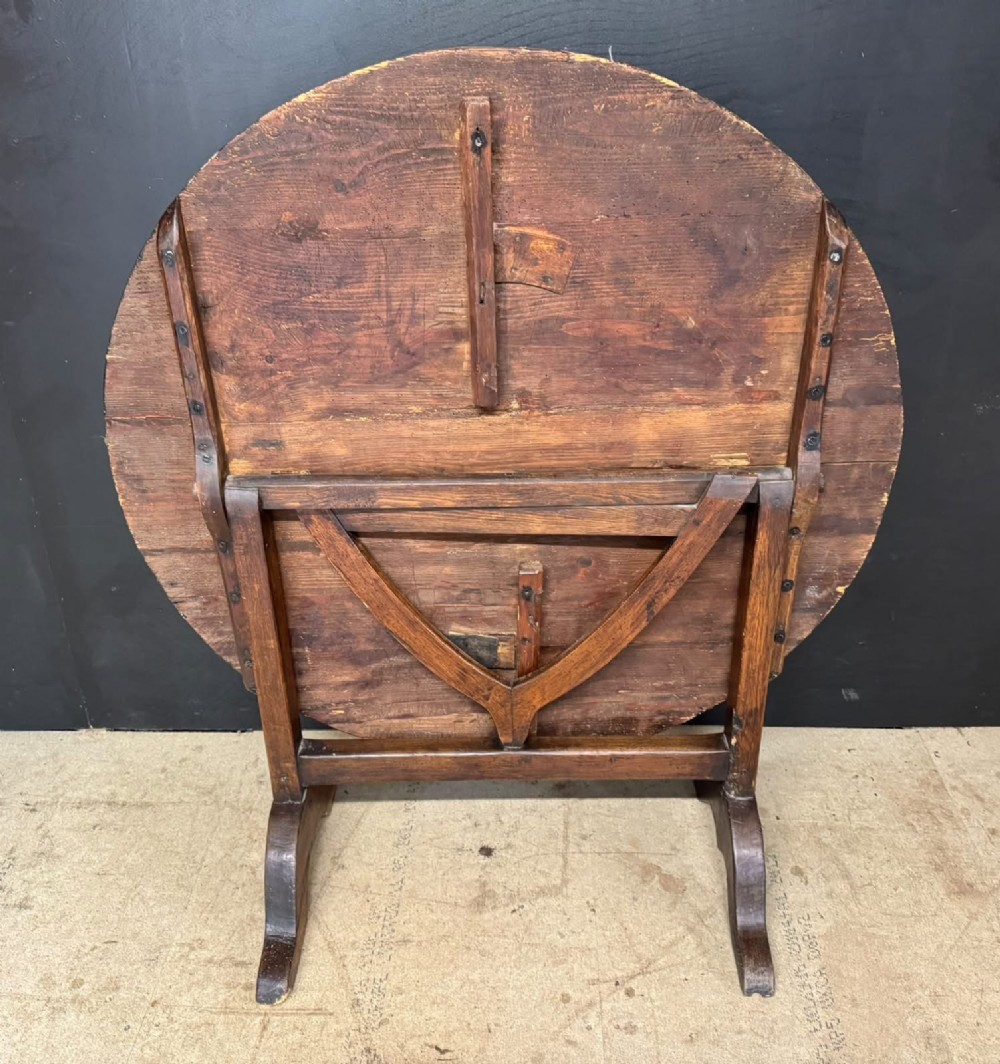 A circular French wine tasting table made of dark warm brown timber shown in a tilted position on a trestle base. View III