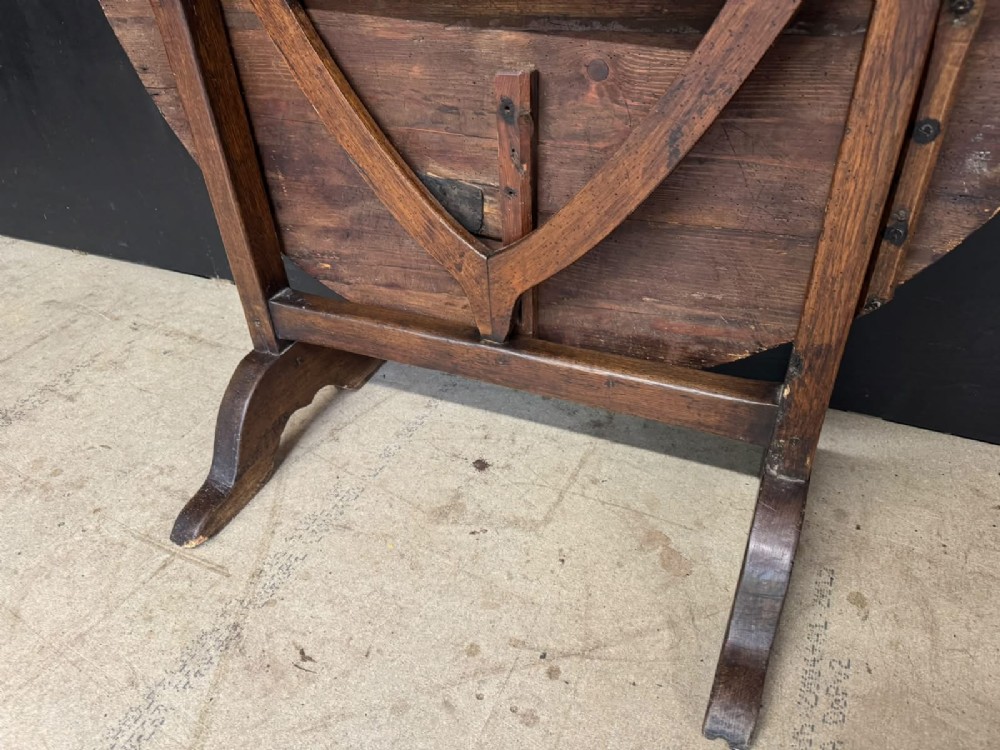 A circular French wine tasting table made of dark warm brown timber shown in a tilted position on a trestle base. View V