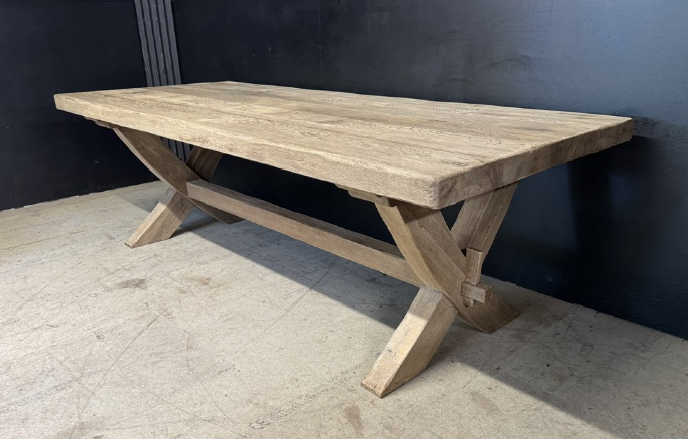 A large solid light oak dining table featuring an X-frame trestle base and a central key-joined stretcher.