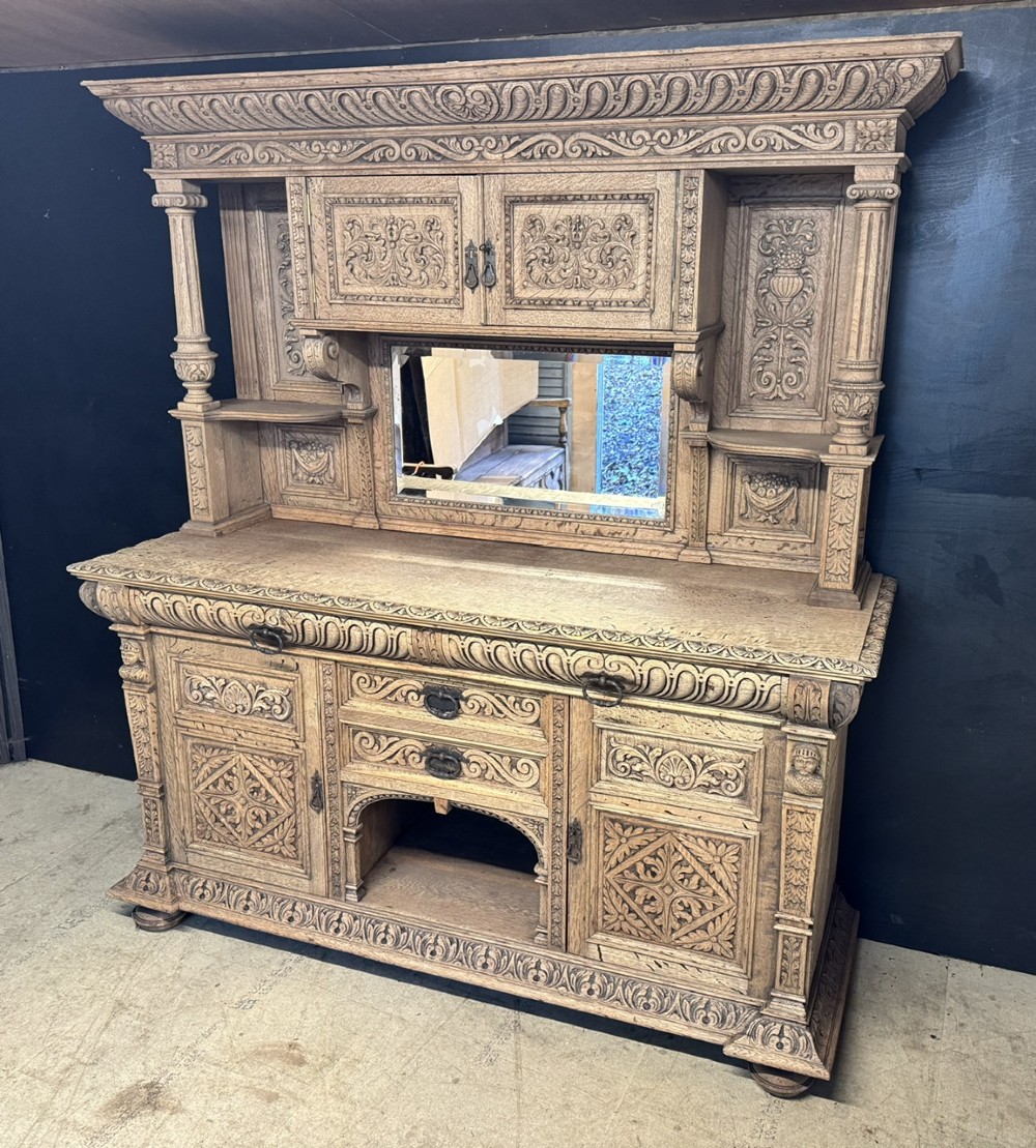 A large carved light oak sideboard with an upper cupboard section, a central mirror plate, turned columns, and detailed relief carvings throughout. View II