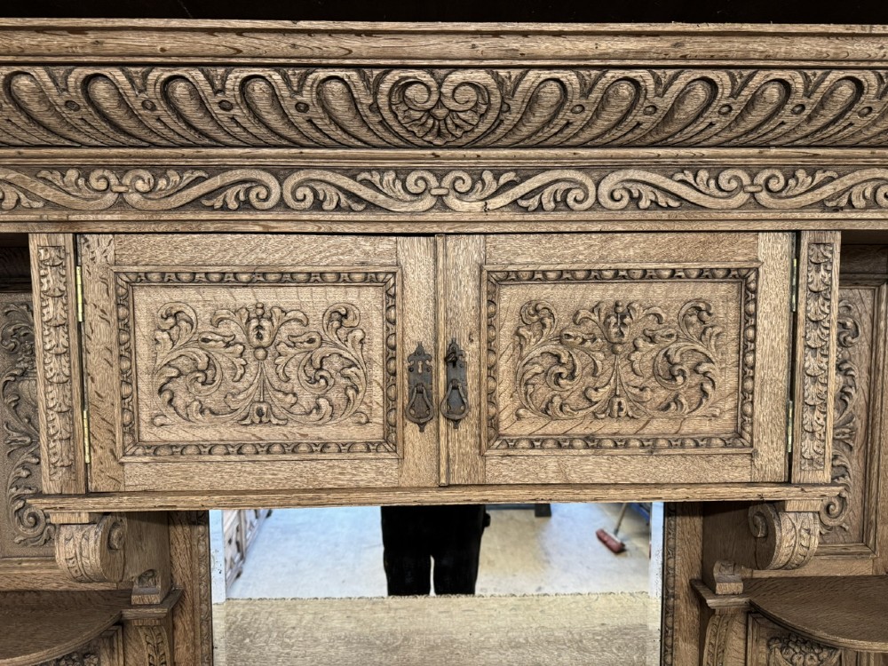 A large carved light oak sideboard with an upper cupboard section, a central mirror plate, turned columns, and detailed relief carvings throughout. View III
