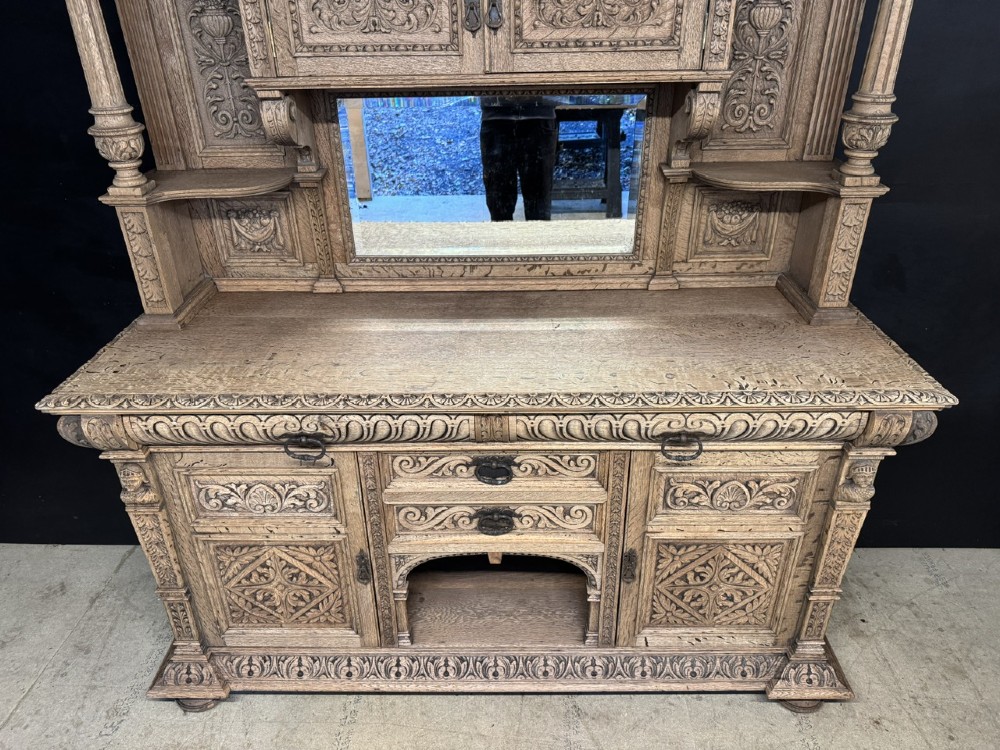 A large carved light oak sideboard with an upper cupboard section, a central mirror plate, turned columns, and detailed relief carvings throughout. View IV
