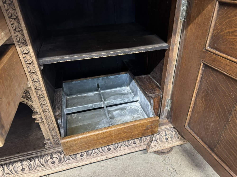 A large carved light oak sideboard with an upper cupboard section, a central mirror plate, turned columns, and detailed relief carvings throughout. View XII